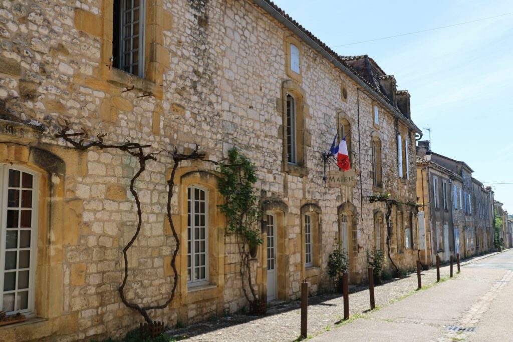 Picturesque view of a historic street in a French village with rustic stone buildings and French flags.