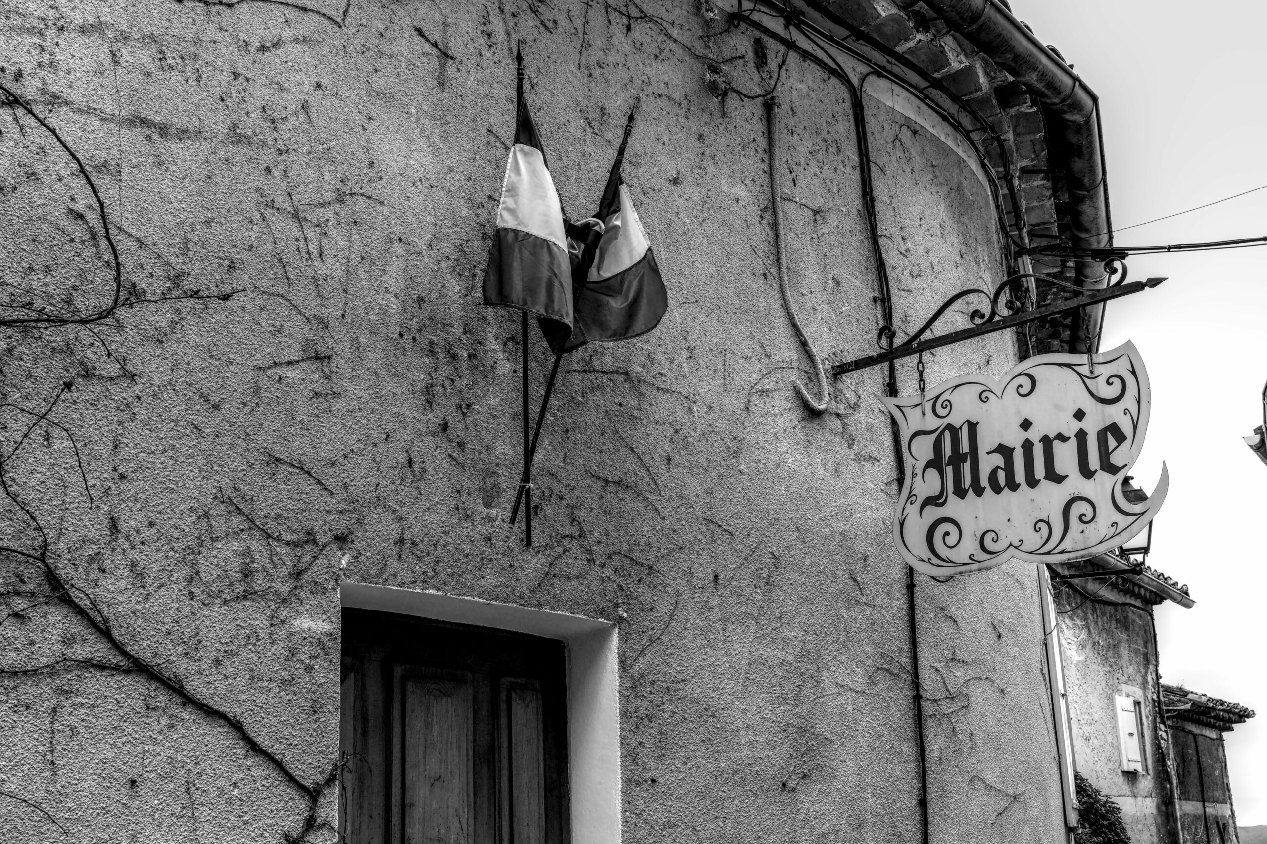 Black and white photo of a French mairie building facade with flags and nostalgic charm.