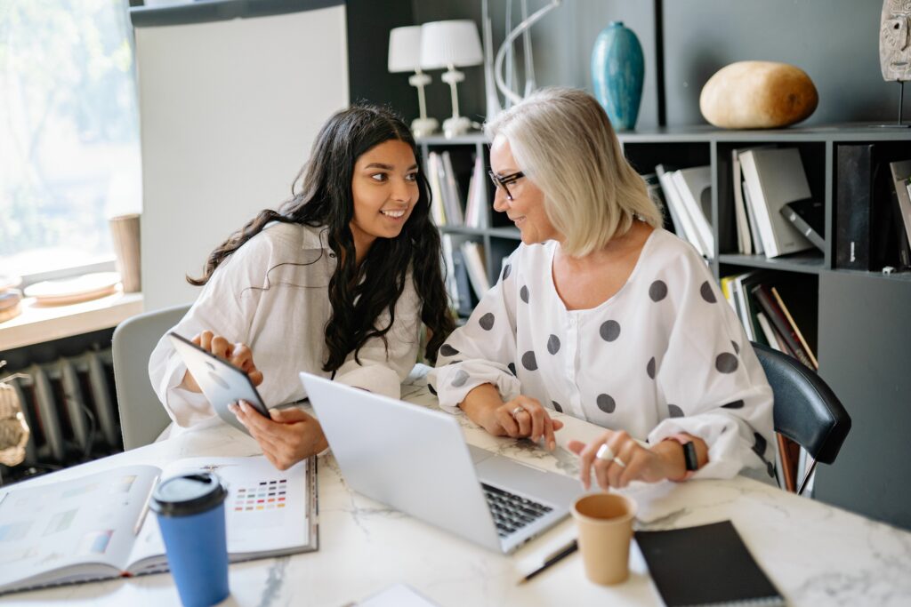 Mon parcours Two businesswomen engaged in a productive meeting around a laptop and tablet in a contemporary office.